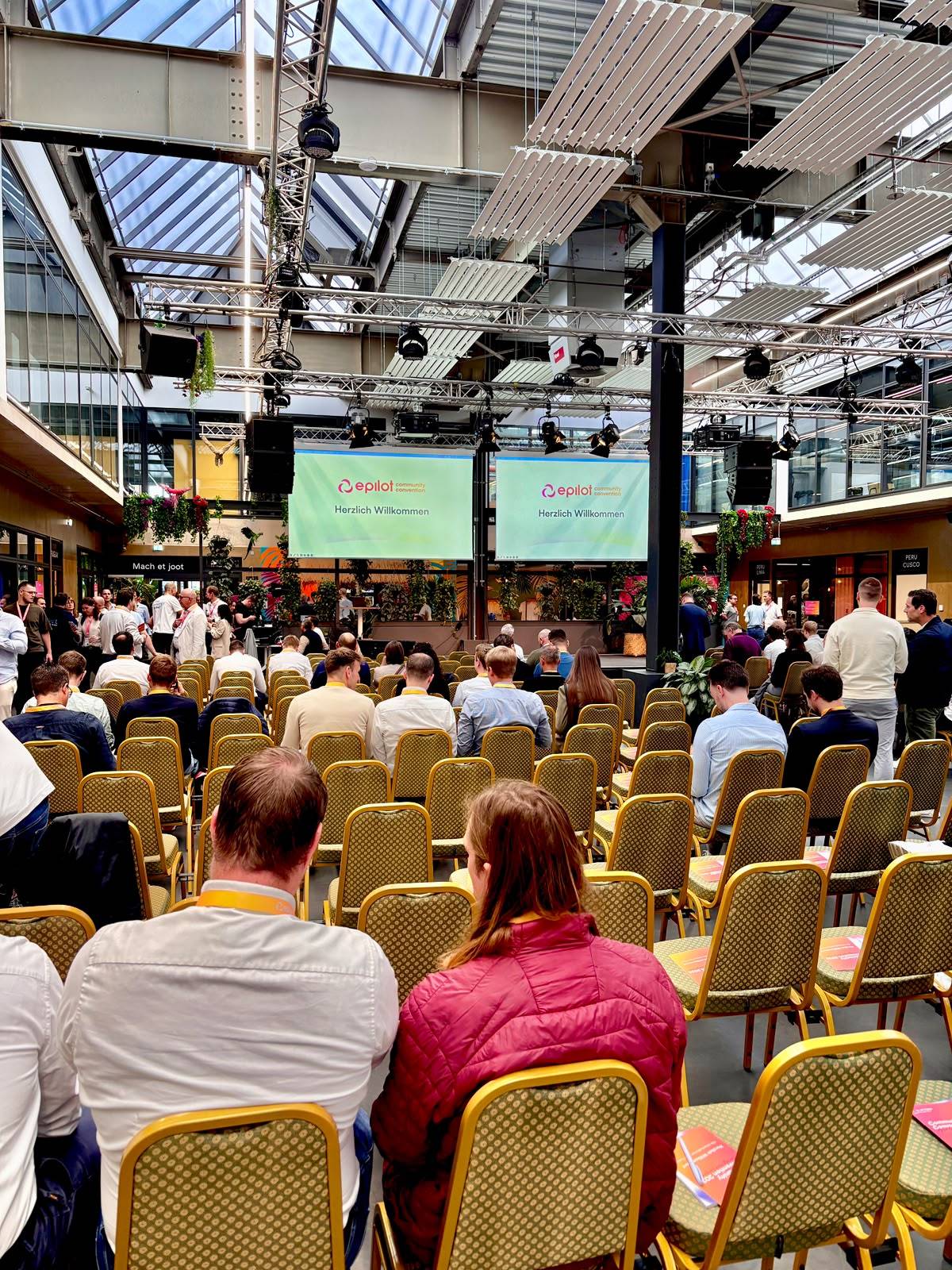 Voll besetzter Saal der epilot Community Convention in Köln, auf den Leinwänden „Herzlich Willkommen“